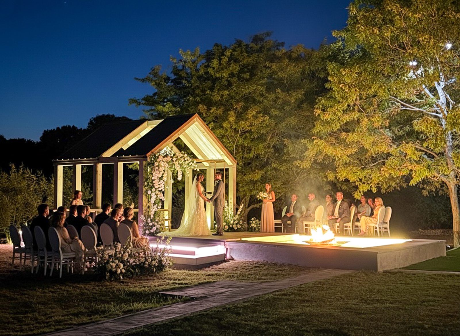 Nighttime wedding with lit pavilion, fire pit, floral arch, blue twilight sky at The Penrose House