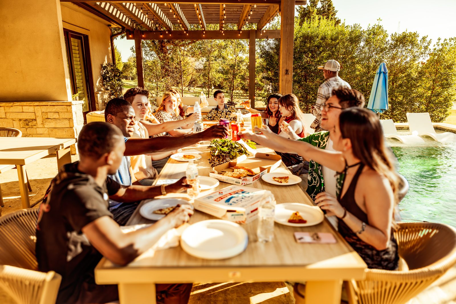 Group al fresco dining with guests toasting poolside, summer casual at The Penrose House