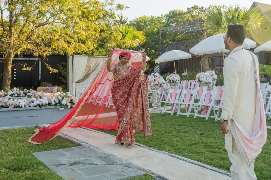 Indian bride in a red saree walking the aisle toward her groom at a backyard wedding ceremony at The Penrose House near Dallas