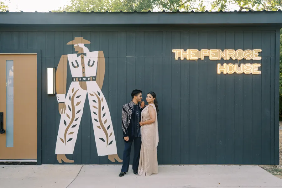Indian couple in reception outfits beside the neon The Penrose House sign at the estate entrance