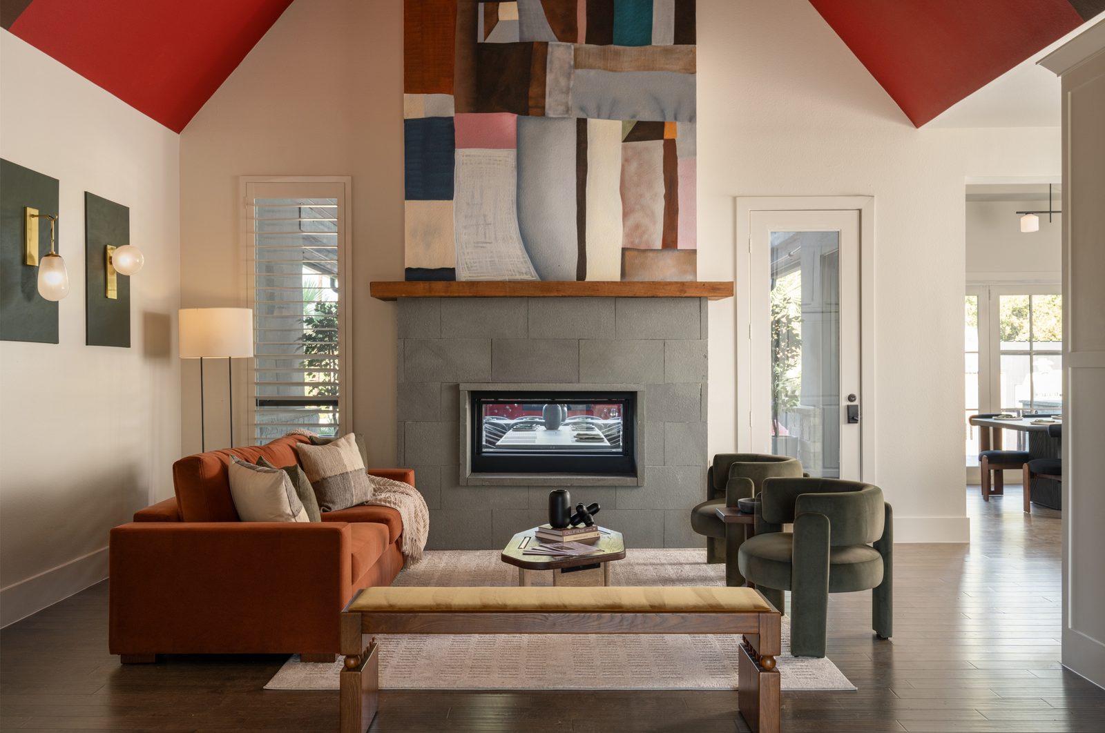 Fireplace with patchwork art, rust sofa, olive chairs, vaulted ceiling at The Penrose House