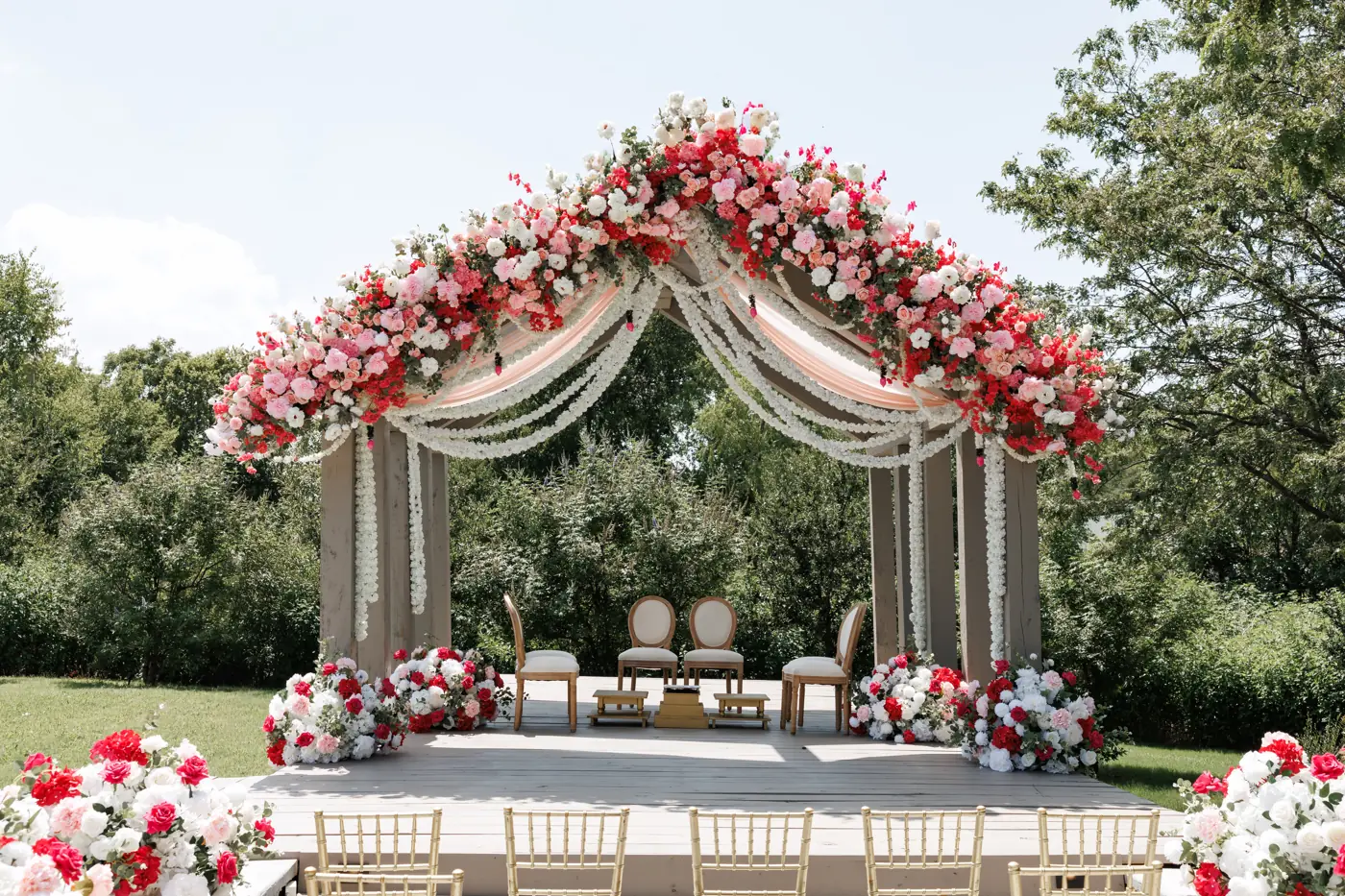 Mandap with red and pink florals and jasmine garlands on the ceremony deck at The Penrose House