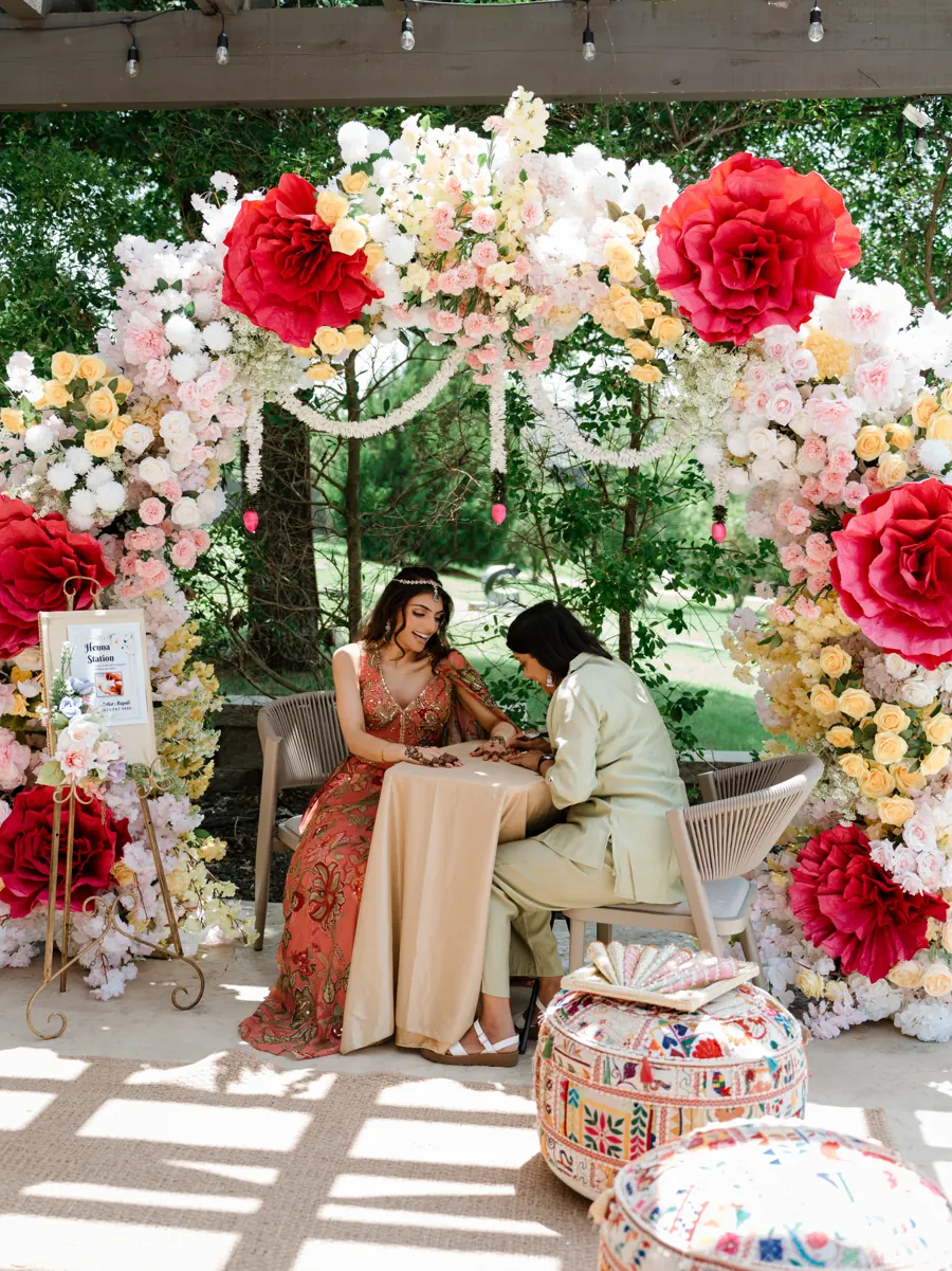 Bride getting mehndi at a henna station under a floral arch on the pergola at The Penrose House
