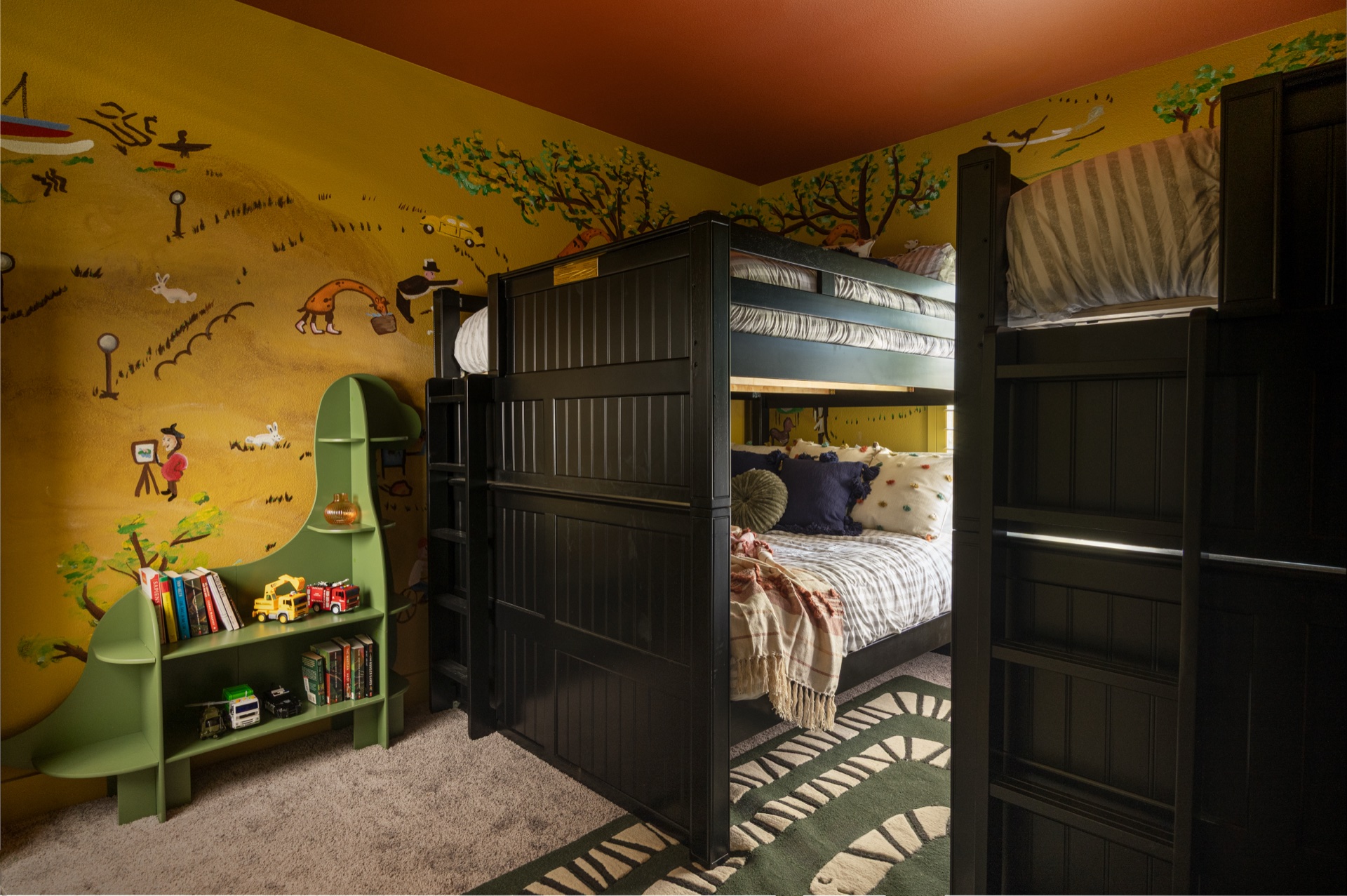 Kids bunk room with yellow safari mural wrapping two walls, bunk beds, green tree-shaped bookshelf and orange ceiling at The Penrose House