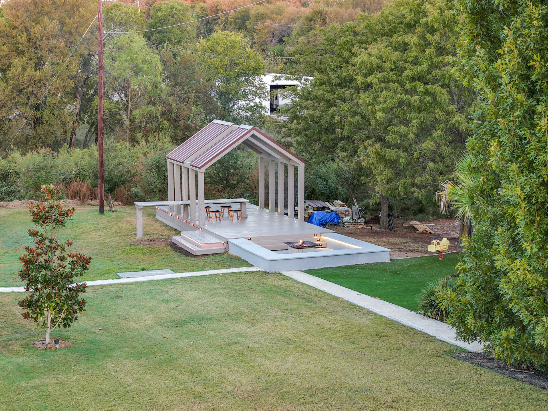 Elevated daylight view of the covered Firepit Pavilion with open firepit deck surrounded by lawn and trees