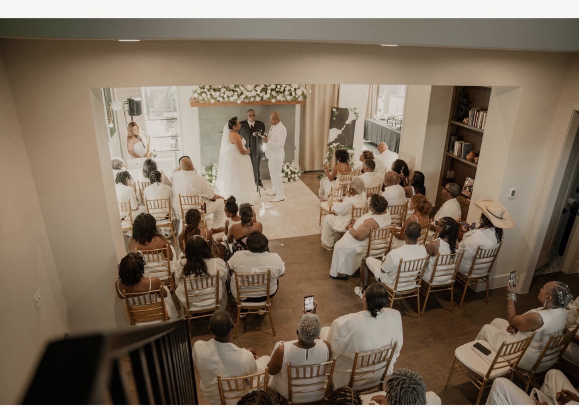 Indoor wedding ceremony with saxophonist on the left and guests dressed entirely in white