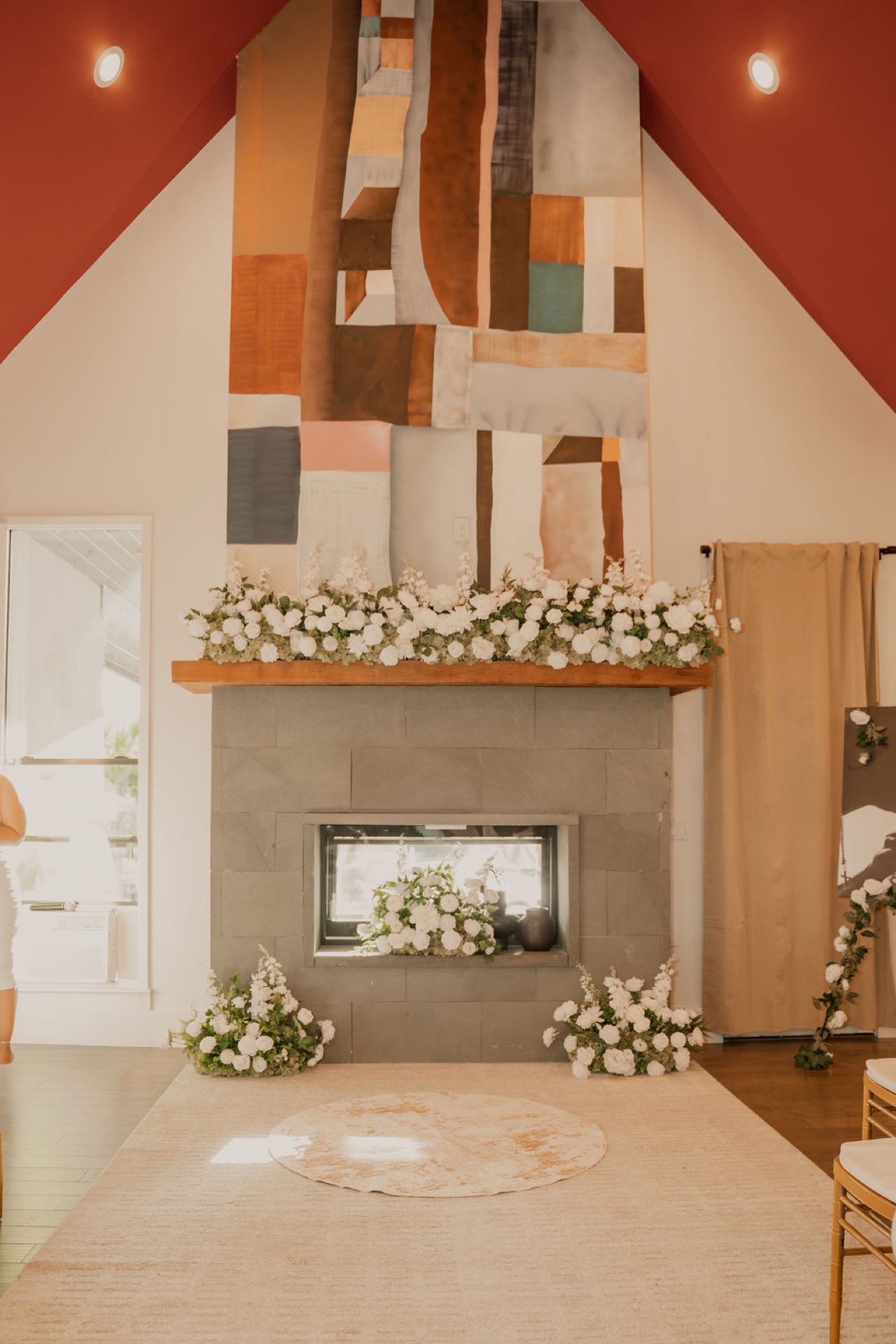 Great room stone fireplace with white floral mantel display beneath the signature art tapestry, set for a ceremony