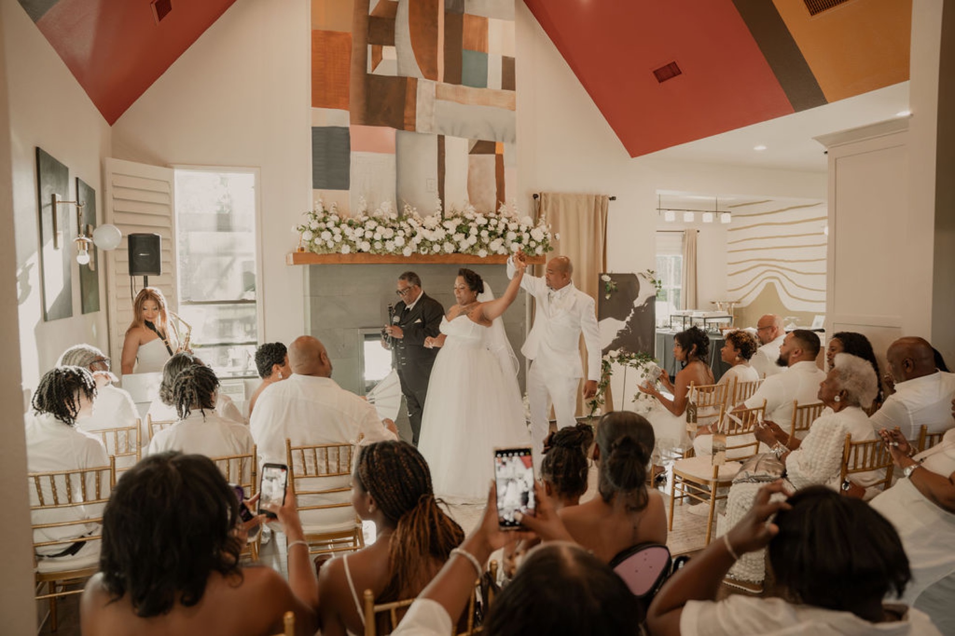 Bride and groom in white with joined hands raised at the end of the ceremony as guests cheer