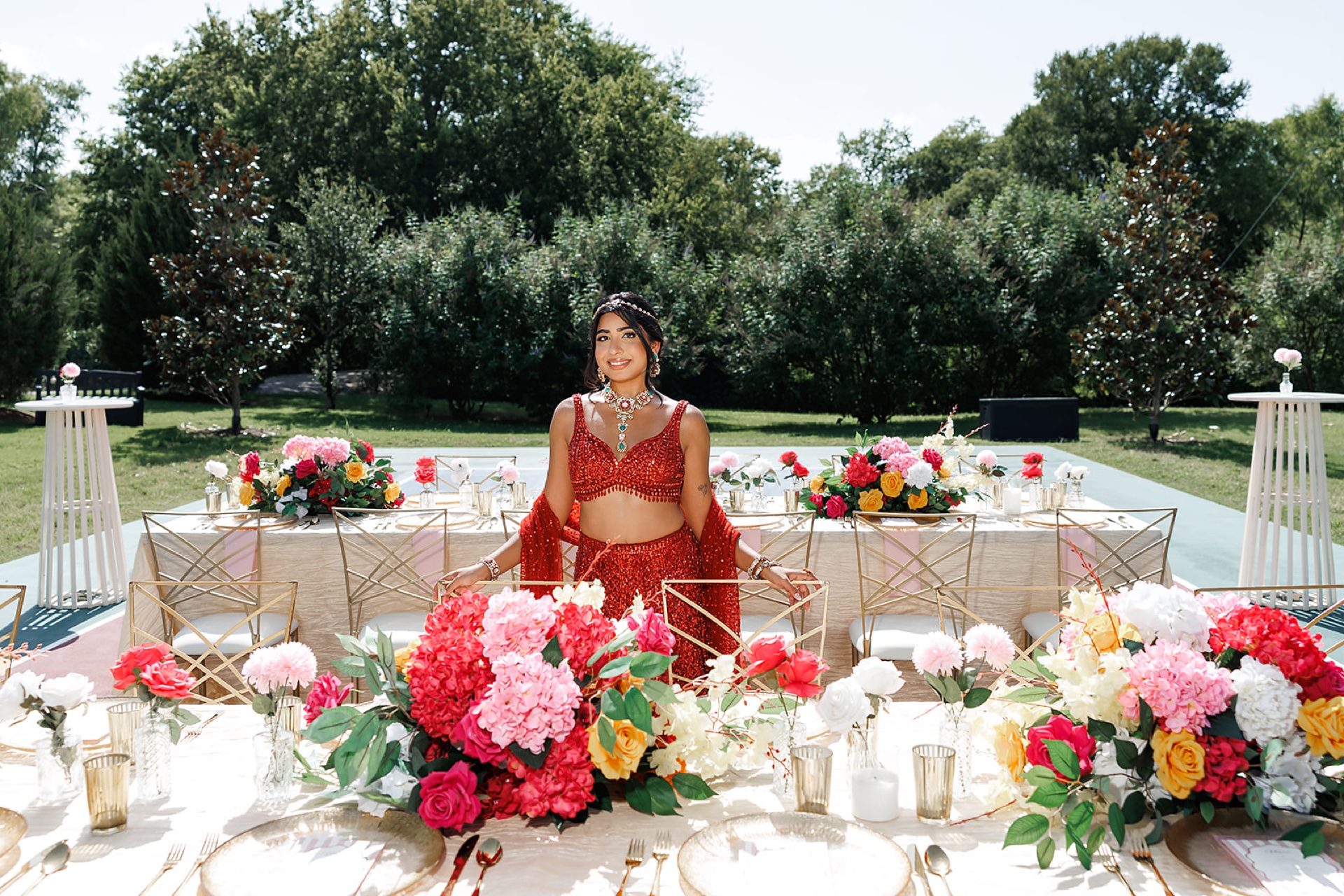 South Asian bride in red sequined lehenga at the head of the reception table with vibrant floral centerpieces