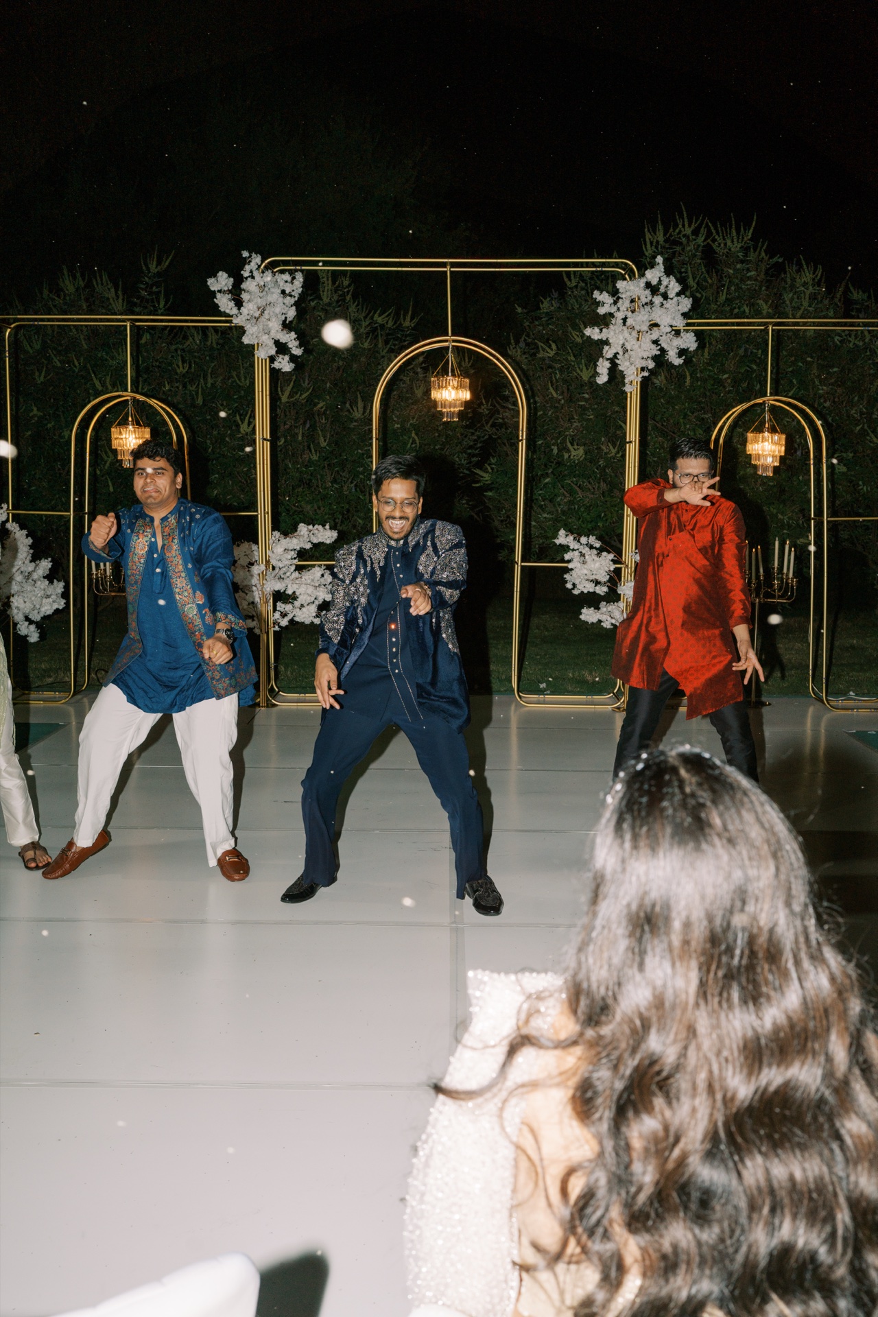 Three men in traditional kurta outfits dancing on the illuminated reception dance floor at night