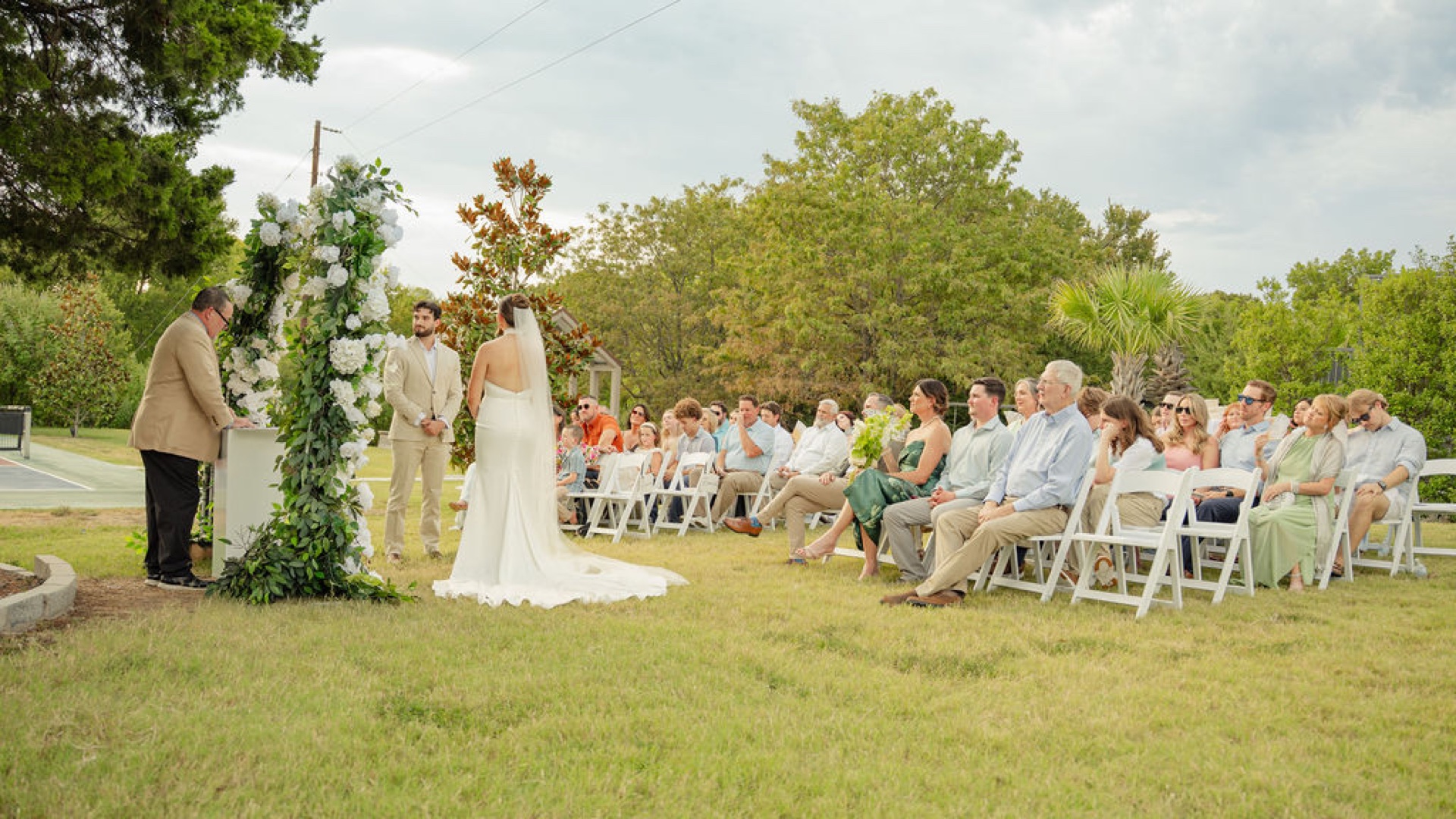 Bride walking the aisle toward the groom at the white floral arch during a real lawn micro-wedding