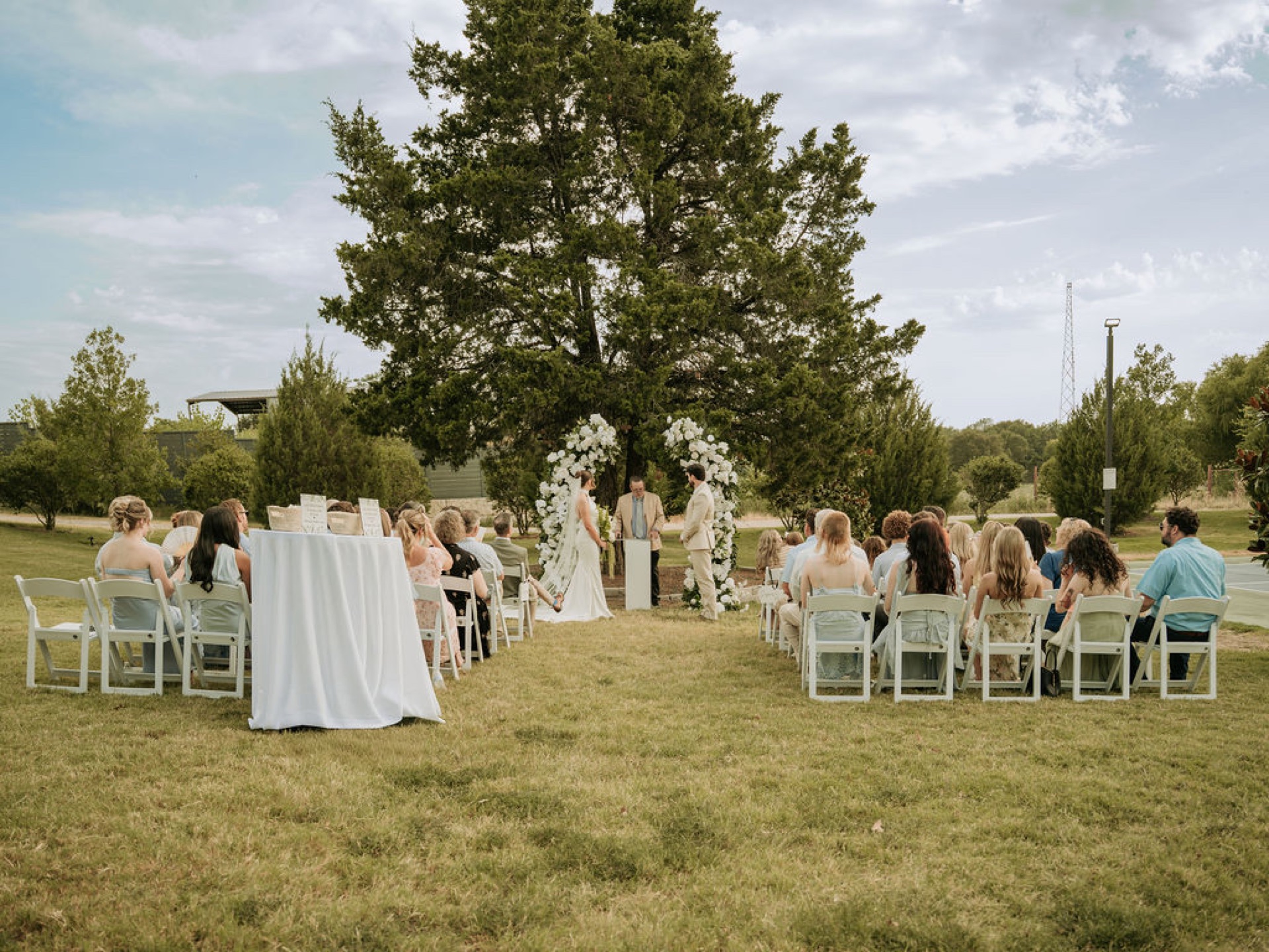 Bride and groom exchanging vows between two white floral arches with guests seated on both sides