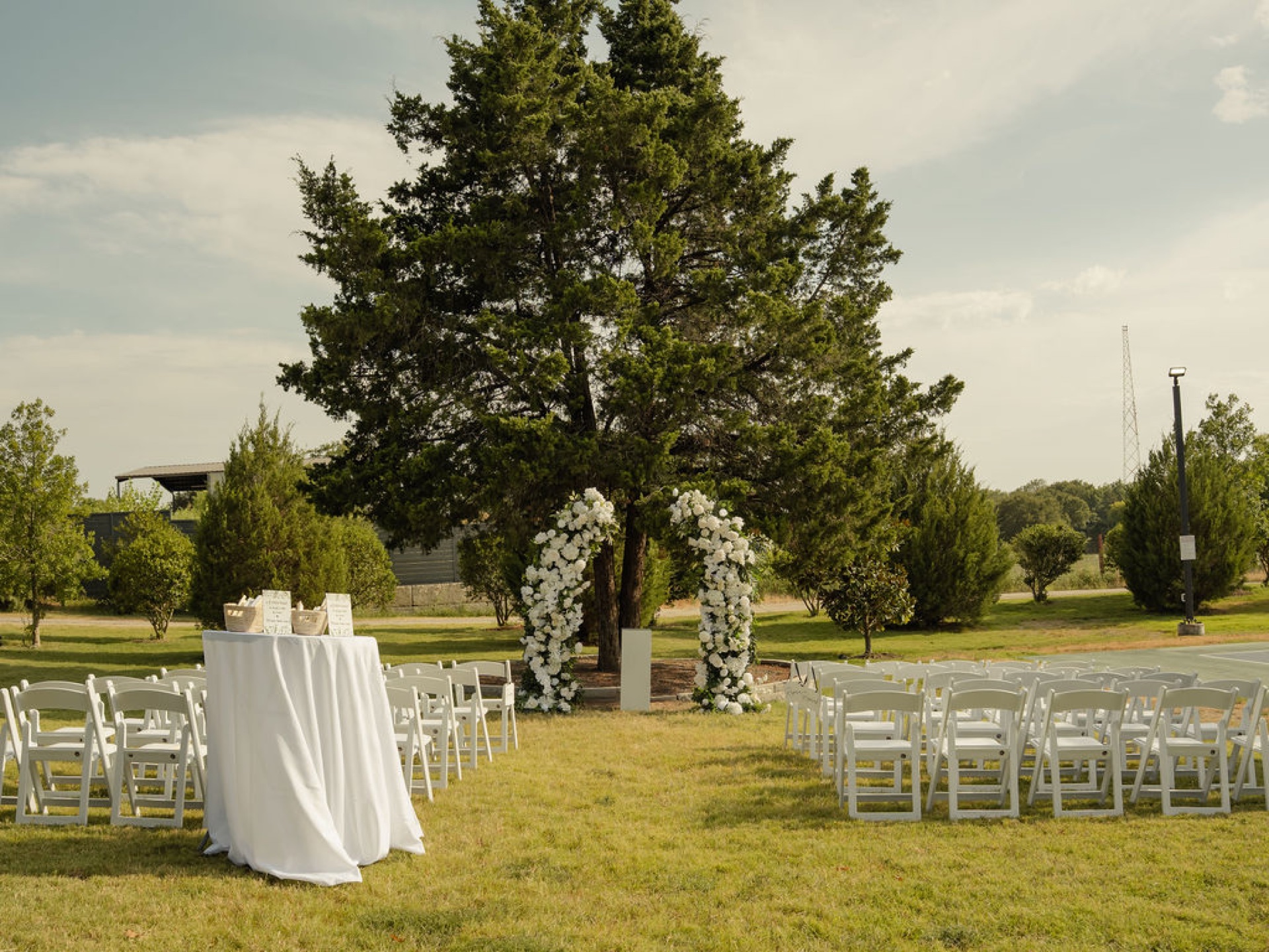 White floral columns flanking the ceremony tree with chairs set for an outdoor wedding, daylight