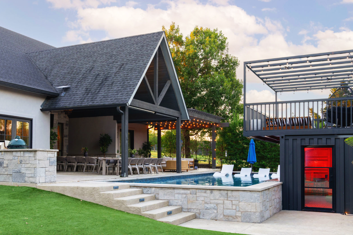 Pool with in-water lounge chairs beside covered outdoor dining patio with string lights at The Penrose House corporate retreat venue