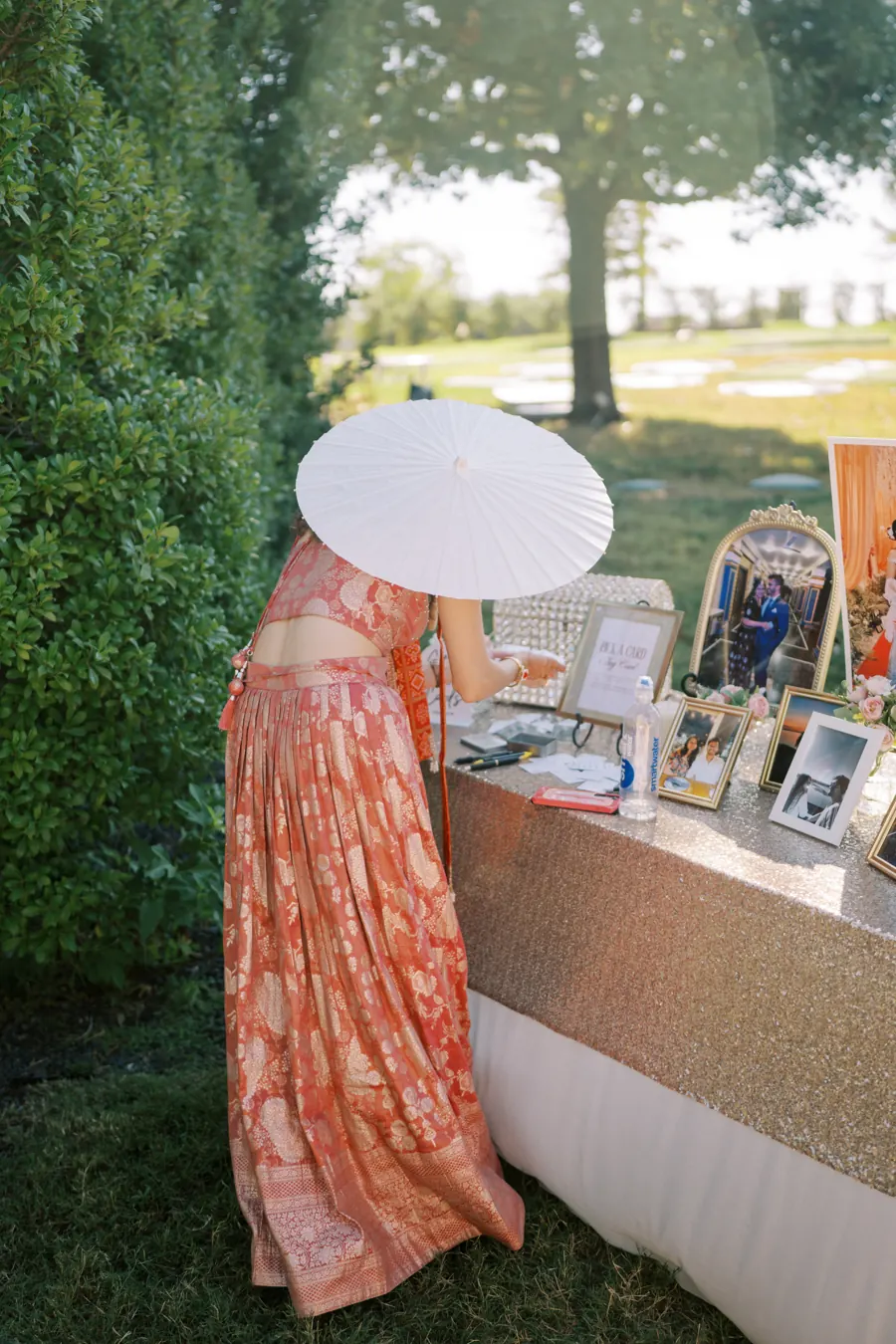 Wedding guest in a lehenga with a paper parasol at the card and photo table on the lawn at The Penrose House